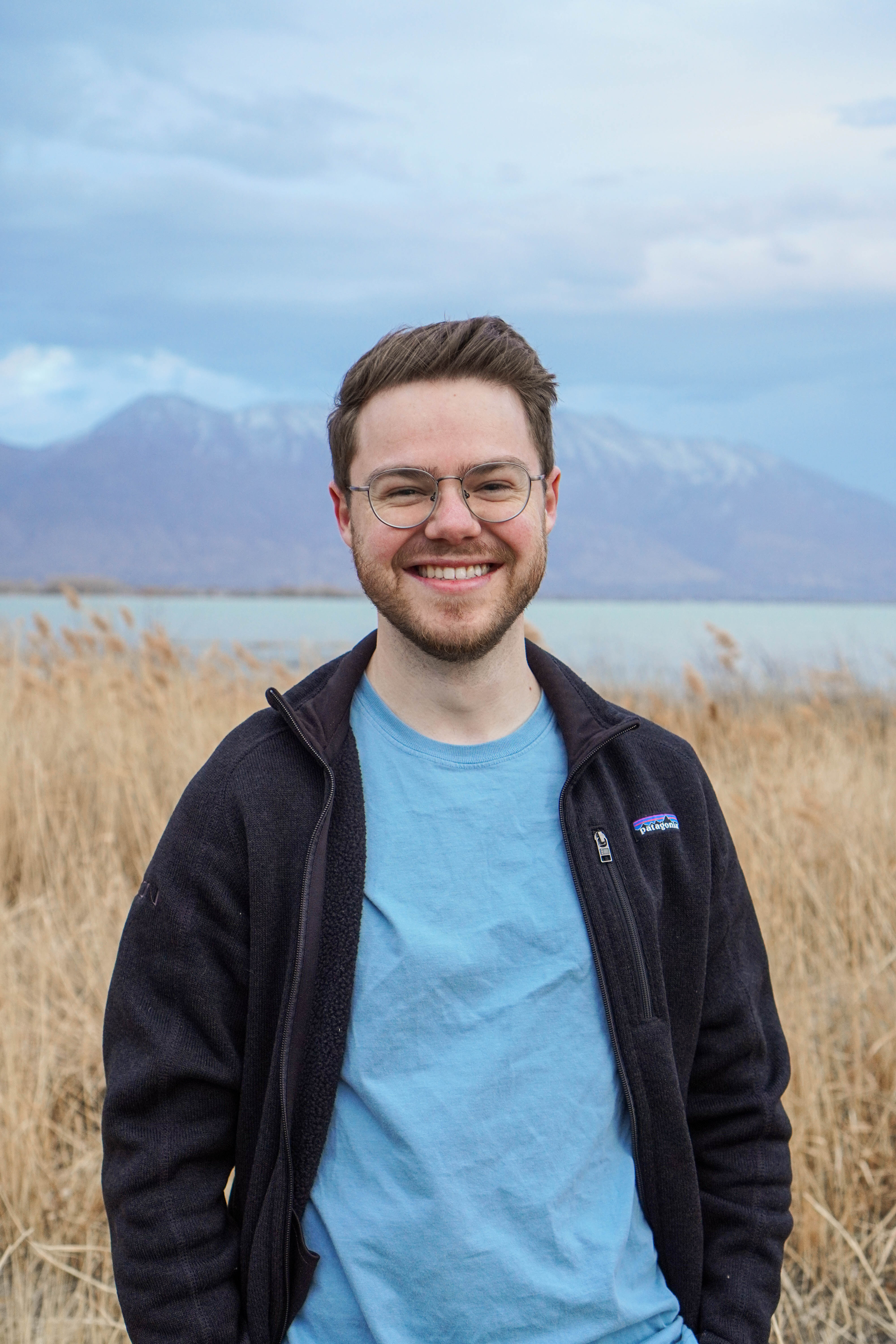 Photo of Zach Kelley smiling with a lake and mountains in the background.